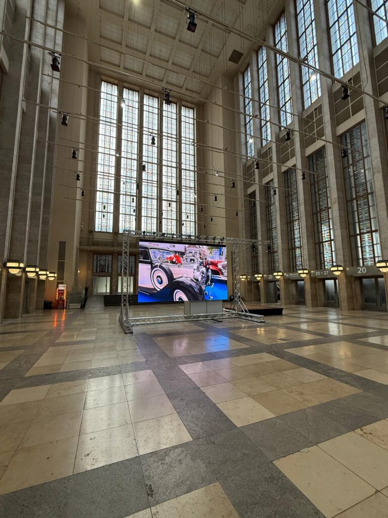 LED-Videowand in Traversenrahmen in einer hohen Halle mit großen Fenstern