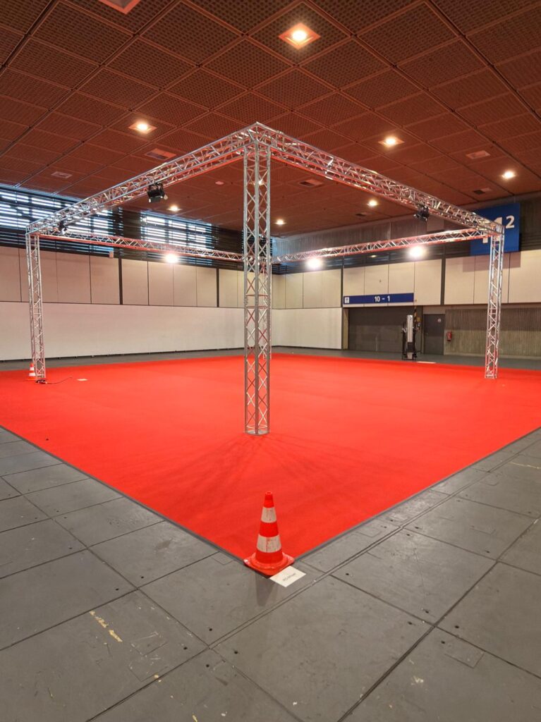Traversenkonstruktion mit Scheinwerfern über rotem Teppich in einer Messehalle