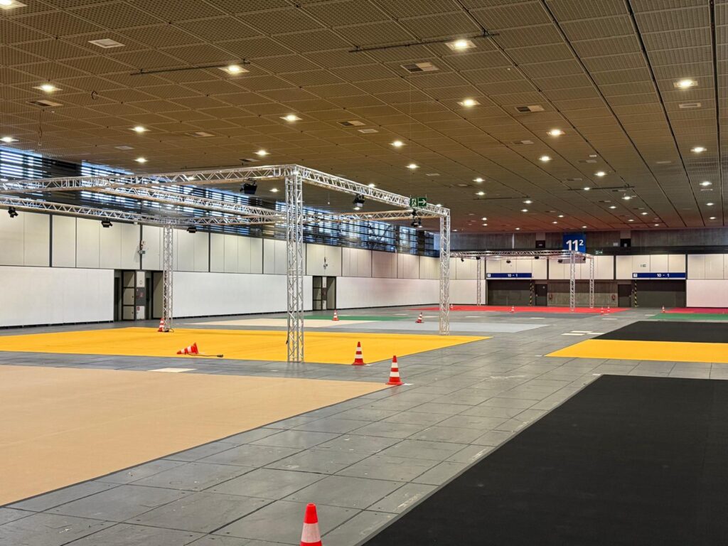 Mehrere Traversenaufbauten mit Scheinwerfern über farbigen Ausstellungsflächen in einer Messehalle